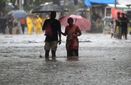 People walk on a flooded road during heavy rain showers in Mumbai on September 4, 2019. (Photo by PUNIT PARANJPE / AFP)