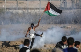 A protester raises a Palestinian flag during clashes with Israeli forces across the border following a demonstration east of Bureij in the central Gaza Strip on September 6, 2019. - Two Palestinian teenagers were killed by Israeli fire in renewed clashes along the Gaza border, the health ministry in the Hamas-run enclave said. (Photo by MAHMUD HAMS / AFP)