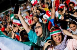 Women wave the Iranian flag from inside the Azadi Stadium where they were allowed for the first time PHOTO: AFP