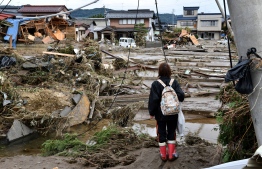 A woman looks at flood-damaged homes in Nagano on October 15, 2019, after Typhoon Hagibis hit Japan on October 12 unleashing high winds, torrential rain and triggered landslides and catastrophic flooding. - Rescuers in Japan worked into a third day on October 15 in an increasingly desperate search for survivors of a powerful typhoon that killed nearly 70 people and caused widespread destruction. (Photo by Kazuhiro NOGI / AFP)