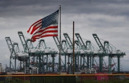 (FILES) In this file photo taken on March 04, 2019 the US flag flies over shipping cranes and containers after a report said the United States and China are close to reaching a major trade deal that would see both sides lower some of the tariffs imposed during an often-bitter trade war, in Long Beach, California. - President Donald Trump on October 11, 2019, hailed breakthrough in his drawn-out trade war with China, saying the two sides had reached an initial deal. At the White House, Trump told reporters the two sides had "come to a very substantial phase one deal." (Photo by Mark RALSTON / AFP)