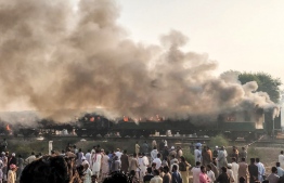 In this handout picture taken and release by Punjab Emergency Service Rescue 1122 on October 31, 2019, residents gather beside the burnt-out train carriages after a passenger train caught on fire near Rahim Yar Khan in Punjab province on October 31, 2019. - At least 65 people were killed and dozens wounded after a passenger train erupted in flames in central Pakistan on October 31, a provincial minister said. (Photo by Handout / Pakistan's Punjab Emergency Service Rescue 1122 / AFP) / 