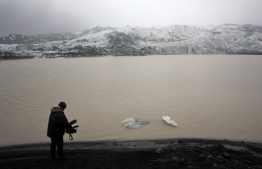 (FILES) This file photo taken on October 16, 2015 shows a cameraman taking pictures of the Solheimajokull glacier where the ice is retreating. - Each October since 2010, now-retired schoolteacher Jon Stefansson has brought students aged around 13 from a school in Hvolsvollur -- a village about 60 kilometres (35 miles) away -- to the glacier to record its evolution. The results are chilling: nestled between two moss-covered mountain slopes, Solheimajokull has shrunk by an average of 40 metres (130 feet) per year in the past decade, according to the students' measurements. (Photo by THIBAULT CAMUS / POOL / AFP)
