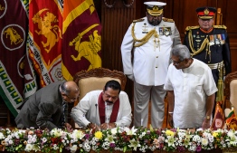Sri Lanka's former president Mahinda Rajapaksa (C sitting) signs documents to take oath as country's Prime Minister while his brother, President Gotabaya Rajapaksa (R) looks on during the swearing-in ceremony in Colombo on November 21, 2019. - Newly elected Sri Lankan President Gotabaya Rajapaksa on November 20 named his brother Mahinda as Prime Minister, cementing the grip on power of a clan credited with brutally crushing the Tamil Tigers a decade ago. (Photo by LAKRUWAN WANNIARACHCHI / AFP)