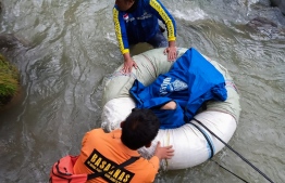 This handout picture taken and released by Indonesia's national search and rescue agency (BASARNAS) on December 24, 2019 shows rescue personnel retrieving a victim after a bus careered into a 150-metre deep ravine and ended up in a river killing dozens, near Perahu Dipo village in Pagar Alam, South Sumatra. - At least two dozen people died and 13 others were injured after a bus plunged into a ravine in Indonesia, police said. (Photo by Handout / BASARNAS / AFP) / 