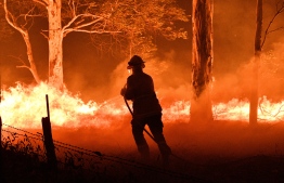 This picture taken on December 31, 2019 shows a firefighter hosing down trees and flying embers in an effort to secure nearby houses from bushfires near the town of Nowra in the Australian state of New South Wales. - Fire-ravaged Australia has launched a major operation to reach thousands of people stranded in seaside towns after deadly bushfires ripped through popular tourist areas on New Year's Eve. (Photo by SAEED KHAN / AFP)