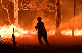 This picture taken on December 31, 2019 shows a firefighter hosing down trees and flying embers in an effort to secure nearby houses from bushfires near the town of Nowra in the Australian state of New South Wales. - Fire-ravaged Australia has launched a major operation to reach thousands of people stranded in seaside towns after deadly bushfires ripped through popular tourist areas on New Year's Eve. (Photo by SAEED KHAN / AFP)