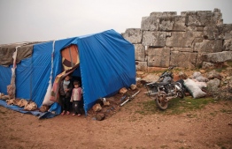 Syrian children, displaced from the western countryside of Aleppo province, stand through the doorway of a tent at the site of ancient ruins where they are encamped for refuge from the rain near the town of Atareb on January 19, 2020. (Photo by Aaref WATAD / AFP)