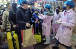 This photo taken on January 22, 2020 shows a staff member (center R) checking body temperature of a passenger at the Yingtan North Railway Station in Nanchang in China's central Jiangxi province.  (Photo by STR / AFP) /