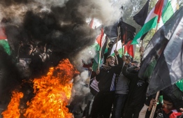 Palestinian demonstrators chant slogans and wave Palestinian flags as they stand by flaming tyres during a protest against US President Donald Trump's expected peace plan proposal in Gaza City on January 28, 2020. (Photo by MAHMUD HAMS / AFP)