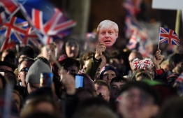 Brexit supporters wave Union flags and a mask of Britain's Prime Minister Boris Johnson as the time reaches 11 O'Clock, in Parliament Square, venue for the Leave Means Leave Brexit Celebration in central London on January 31, 2020, the moment that the UK formally leaft the European Union. - Brexit supporters gathered outside parliament on Friday to cheer Britain's departure from the European Union following three years of epic political drama -- but for others there were only tears. After 47 years in the European fold, the country leaves the EU at 11:00pm (2300 GMT) on Friday, with a handful of the most enthusiastic supporters gathering opposite the Houses of Parliament 12 hours before the final countdown. PHOTO: DANIEL LEAL-OLIVAS / AFP
