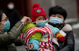 A woman (L) puts a protective mask on a child at the Jingshan park in Beijing on February 2, 2020. PHOTO: NICOLAS ASFOURI / AFP