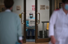 A medical worker wearing protective gear (C) waits to take the temperature of people in an entrance of Princess Margaret Hospital in Hong Kong on February 4, 2020. - Hong Kong on February 4 become the second place outside of the Chinese mainland to report the death of a patient being treated for a new coronavirus that has so far claimed more than 400 lives. (Photo by Anthony WALLACE / AFP)