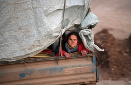 A displaced Syrian girl rides in the back of a truck on the way to Deir al-Ballut camp in Afrin's countryside along the border with Turkey, on February 19, 2020 after fleeing regime offensive on the last major rebel bastion in the country's northwest. (Photo by Rami al SAYED / AFP)