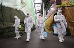 Market workers wearing protective gear spray disinfectant at a market in the southeastern city of Daegu, South Korea on February 23, 2020 as a preventive measure after the COVID-19 coronavirus outbreak. (Photo by - / YONHAP / AFP)