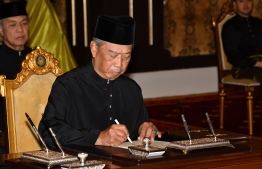 This handout from Malaysia's Department of Information taken and released on March 1, 2020 shows Malaysia's Prime Minister Muhyiddin Yassin signing documents after taking the oath as the country's new leader at the National Palace in Kuala Lumpur. (Photo by FAMER ROHENI / Malaysia's Department of Information / AFP) / 