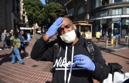 Cameron Nightingale adjusts his mask and gloves, a precaution to protect himself from  coronavirus, while walking by cable car in San Francisco, California on February 27, 2020. - California said it was monitoring some 8,400 people for the new coronavirus, after officials confirmed a woman had contracted the disease without travelling to outbreak-hit regions. The Centers for Disease Control and Prevention (CDC) said it doesn't know how the woman -- who had not travelled or been in contact with another coronavirus patient -- got sick. (Photo by Josh EDELSON / AFP)