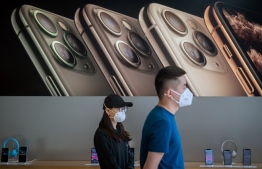 In this picture taken on March 11, 2020 customers wearing face masks as a preventive measure against the COVID-19 coronavirus are seen inside of an Apple shop in Beijing. (Photo by NICOLAS ASFOURI / AFP)