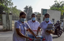 Nurses wearing facemasks cross a road as they push a trolley filled with leaflets outside the entrance of Sri Lanka's Infectious Diseases Hospital near Colombo on March 17, 2020. (Photo by LAKRUWAN WANNIARACHCHI / AFP)