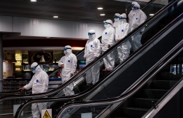 Medical staff wearing protective suits ride down an escalator at Moscow's Sheremetyevo airport on March 18, 2020. - President Vladimir Putin on March 17 said the coronavirus situation was "under control" in Russia and outbreaks of infection had been contained. The country is closing its borders to foreigners from March 18, and cultural and sports events have been suspended. (Photo by Dimitar DILKOFF / AFP)