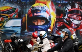 (FILES) In this file photo taken on March 2, 2020, a woman, wearing a facemask amid concerns over the COVID-19 novel coronavirus, checks her mobile phone in front of a poster outside the Formula One Vietnam Grand Prix merchandise store in Hanoi. - Vietnam Formula One Grand Prix has been postponed due to coronavirus - organisers said on March 13, 2020. (Photo by Nhac NGUYEN / AFP)