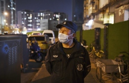 A security guard wearing a facemask amid concerns over the spread of the COVID-19 novel coronavirus, watches over the entrance to a residential community in Beijing on March 20, 2020. (Photo by GREG BAKER / AFP)
