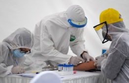 Health workers, wearing protective clothing amid concerns of the spread of the COVID-19 coronavirus, take a blood sample from a resident at a makeshift rapid testing centre near the Bach Mai hospital in Hanoi on March 31, 2020. (Photo by Nhac NGUYEN / AFP)