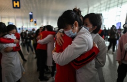 Medical staff from Jilin Province (in red) hug nurses from Wuhan after working together during the COVID-19 coronavirus outbreak during a ceremony before leaving as Tianhe Airport is reopened in Wuhan in China's central Hubei province on April 8, 2020. - Thousands of Chinese travellers rushed to leave COVID-19 coronavirus-ravaged Wuhan on April 8 as authorities lifted a more than two-month prohibition on outbound travel from the city where the global pandemic first emerged. (Photo by Hector RETAMAL / AFP)