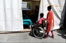This photograph taken on April 7, 2020 shows wife of 38-year-old patient Upender Safi (C) pushing his wheelchair at a night shelter setup by Delhi government outside the All India Institute of Medical Sciences (AIIMS) during a government-imposed nationwide lockdown as a preventive measure against the COVID-19 coronavirus, in New Delhi. - The capacity of medical facilites around the world has been stretched by the surge of COVID-19 patients as outbreaks worsen in many countries. It can cause people with other life-threatening diseases to miss out on vital care -- especially in places like India, where healthcare systems are shakier. Dozens of people with serious medical conditions are camped outside India's national medical institute in tents set up by the Delhi government. (Photo by Prakash SINGH / AFP) / 
