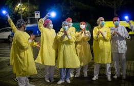 Heathcare workers wearing face masks and protective suits acknowledge applause outside the Hospital de Barcelona to people in his houses on April 13, 2020 in Barcelona, during a national lockdown to prevent the spread of the COVID-19 disease. - Spain reopened parts of its coronavirus-stricken economy on Monday as slowing death tolls in some of the worst-hit countries boosted hopes the outbreak may be peaking and lockdowns could soon be eased. (Photo by Josep LAGO / AFP)