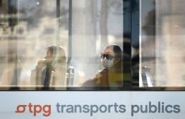 A woman wearing a protective mask looks on from the window of a tram in Geneva on April 16, 2020, during the lockdown due to the novel coronavirus, COVID-19. (Photo by Fabrice COFFRINI / AFP)