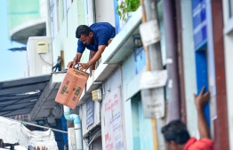 Chucking supplies out of windows - a go-down worker hands down a case of product for delivery. Dozens like him work tirelessly in the unforgiving April sun to ensure that other frontline workers, ordinary residents, across the archipelago receive the supplies they need. PHOTO: AHMED AWSHAN ILYAS / MIHAARU