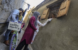 Palestinian activists and volunteers from the Women's Program Center distribute crafts and reading material to children confined at home due to the novel coronavirus pandemic, in the central Deir al-Balah refugee camp in the Gaza Strip, on April 12, 2020. (Photo by MAHMUD HAMS / AFP)
