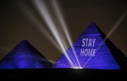 A picture taken on April 18, 2020 show the Great pyramids lighten-up with blue light and reading with a laser projection the message "Stay Home" on the Giza plateau outside the Egyptian capital of Cairo, on the world heritage day, as the country fights against the spread of the COVID-19, (the novel coronavirus). (Photo by Khaled DESOUKI / AFP)