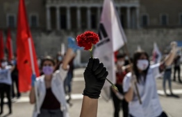 A member of the Greek Labour Union (PAME), holds a red carnation during a protest in front of the Greek Parliament during the Labour Day demonstration in Athens on May 1, 2020, as the Greek government asked unions to delay public rallies by more than a week, but leading union GSEE called for a general strike to coincide with May Day. - Workers were forced to scale back May Day rallies around the world on May 1, 2020, because of coronavirus lockdowns, although some pushed on with online events and others hit the streets in face masks. (Photo by Aris MESSINIS / AFP)