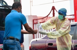 Health worker dressed in PPE offers sanitizer to a man, in front of Iskandhar school in the Maafannu district,  presumably before conducting a COVID19 test. PHOTO: MIHAARU 