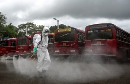 A police officer wearing protective gear sprays disinfectant on special buses organised by Sri Lanka police to transport stranded citizens back to their hometowns after the government ended a lockdown which was imposed as a preventive measure against the COVID-19 coronavirus, at a public ground in Kalutara some 43 kms from Colombo on May 16, 2020. (Photo by LAKRUWAN WANNIARACHCHI / AFP)