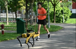(FILES) In this file photo taken on May 8, 2020, a man jogs past a four-legged robot called Spot, which broadcasts a recorded message reminding people to observe safe distancing as a preventive measure against the spread of the COVID-19 coronavirus, during its two-week trial at the Bishan-Ang Moh Kio Park in Singapore. PHOTO: AFP