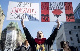 A woman holds signs as demonstrators block vehicular traffic along Wellington Street in Ottawa at a rally in solidarity with Wet'suwet'en hereditary chiefs opposed to the Costal GasLink Pipeline, on Monday, Feb. 24, 2020. THE CANADIAN PRESS/Justin Tang