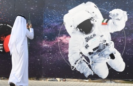 (FILES) In this file photo taken on September 25, 2019 a man takes a picture of an illustration depicting an astronaut with the Emirati national flag outside Mohammed Bin Rashid Space Centre (MBRSC) in Dubai. - The first Arab space mission to Mars, set for launch next month to study the Red Planet's atmosphere, is designed to inspire the region's youth and pave the way for scientific breakthroughs, officials said on June 9, 2020. (Photo by KARIM  SAHIB / AFP)
