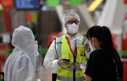 An employee in full protective gear checks the temperature of passengers arriving to check in for their flight bound for Beijing at the Barajas airport in Madrid on June 20, 2020. (Photo by PIERRE-PHILIPPE MARCOU / AFP)