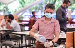 A server, donning a face mask and gloves, serves water in a cafe' as authorities lift restrictions across Male' City, entering the 'new normal'. PHOTO/MIHAARU