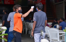 A server takes a customer's temperature before admitting him into a cafe'. PHOTO: NISHAN ALI / MIHAARU