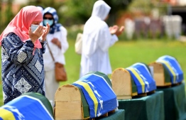 Bosnian Muslim women, survivors of massacre in Western-Bosnian town of Prijedor in 1992, pray and mourn wearing a protective mask, near caskets of their relatives, in the village of Kamicani, on July 20, 2020. - Only 6 out of 30 identified bodies were put to final rest in a local cemetery in Kamicani. Bodies are identified as those belonging to Bosnian non-Serbs that went missing in 1992, only to be found buried in several mass grave locations, years after the war ended. (Photo by ELVIS BARUKCIC / AFP)