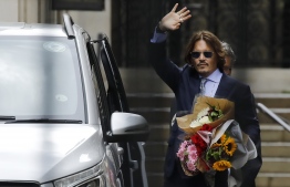US actor Johnny Depp gestures holding a bunch of flowers as he leaves after a hearing in his libel trial against News Group Newspapers (NGN), at the High Court in London, on July 24, 2020. - Depp is suing the publishers of The Sun and the author of the article for the claims that called him a "wife-beater" in April 2018. Johnny Depp's legal team played an anonymous tipster's video at his libel trial Friday aimed at proving ex-wife Amber Heard had a violent streak and once beat up her sister. (Photo by Tolga AKMEN / AFP)