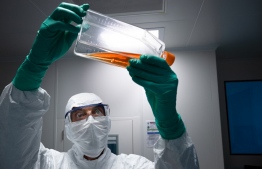 A lab technician in Personal Protective Equipment (PPE) looks at a reagent bottle before performing vaccine tests at a French pharmaceutical company Sanofi's laboratory in Val de Reuil on July 10, 2020. (Photo by JOEL SAGET / AFP)