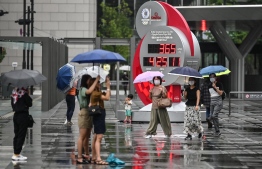 People wearing face masks walk past a countdown clock for the postponed Tokyo 2020 Olympic and Paralympic Games in Tokyo on July 23, 2020. (Photo by Charly TRIBALLEAU / AFP)
