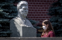 A woman wearing a face mask to protect against the coronavirus disease walks past a bust of Soviet leader Joseph Stalin by the Kremlin wall in downtown Moscow on July 30, 2020. (Photo by Yuri KADOBNOV / AFP)