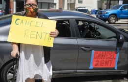 Ady Carrillo poses in front of her car with a sign asking to "Cancel Rent" during the  "Cancel Rent" Protest and Caravan in Chinatown, August 10 2020, in Los Angeles, California. - The "Cancel Rent" movement is gathering steam with protests across the US as Americans hit hard by the coronavirus pandemic pile up debts. Activists want landlords to suspend rent obligations for those in the most dire straits, having lost their jobs in the economic chaos sparked by the virus crisis. (Photo by VALERIE MACON / AFP)