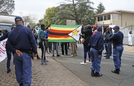 South African police stand near the entrance to the Zimbabwean Embassy during a picket against the government of Zimbabwe's alleged state corruption, media freedom and the deteriorating in Pretoria on August 7, 2020. (Photo by Phill Magakoe / AFP)